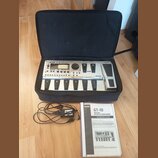 V černé přepravní tašce se nachází stříbrný kytarový procesor s nápisem BOSS GT-10 GUITAR EFFECTS PROCESSOR. Zařízení má displej, ovládací knoflíky a…