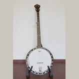 Banjo s bílou membránou a kovovým rímcem, umístěné na černém stojanu. Na hlavě hředu je zlatý nápis „Epiphone“. Uprostřed membrány je viditelné logo…