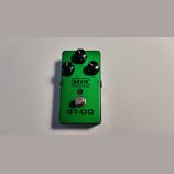 Zelený kytarový efekt s kovovým šasi. Na horní straně jsou tři černé ovládací knoflíky s popisky OUTPUT, TONE a GAIN. Uprostřed je logo MXR a nápis C…