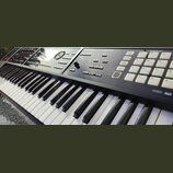 Černý digitální klavír s bílými a černými klávesami. Na ovládacím panelu jsou viditelné nápisy ARPEGGIO/RHYTHM, SEQUENCER a SAMPLER, množství bílých…