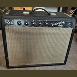 Kytarový zesilovač v černém krytu s béžovou textilní mřížkou. Na ovládacím panelu je nápis Princeton Amp a Fender Electric Instrument Co., dále označ…