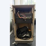 Otevřený transportní rack na kolečkách, v němž jsou namontovány dvě černé zařízení. Horní jednotka nese nápis Soundcraft MINI STAGEBOX 32 a má zapoje…