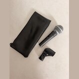 Na fotografii je černý bezdrátový mikrofon s kovovou mřížkou, na jeho těle je nápis SHURE SM58. Vedle mikrofonu je černý kožený obal a černý plastový…