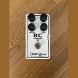 Bílý kytarový efekt s nápisy RC -booster a Xotic Effects CALIFORNIA. Na horní straně jsou čtyři černé otočné knoflíky s popisky GAIN, TREBLE, VOLUME…