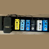 Sada efektů pro kytaru na černém pedalboardu. Zleva jsou vidět černé pedál s nápisem VOLWAH a šest barevných pedálů značky Rowin: žlutý DELAY, světle…