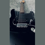 Černá elektrická kytara s tvarem typu Stratocaster a hnědým hmatníkem. Nástroj má jeden viditelný snímač typu humbucker v pozici u mostu a chromovaný…