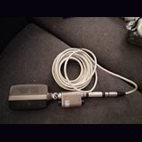 Stříbrný mikrofon s kovovou mřížkou a připojeným bílým kabelem. Na těle mikrofonu je viditelný nápis: „AKG“, „MADE IN AUSTRIA“, „VIENNA“. Povrch vyka…
