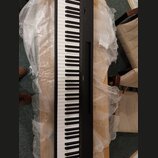 Černý digitální klavír s bílými a černými klávesami. Na pravé straně korpusu je viditelný nápis YAMAHA. Nástroj leží na dřevěném povrchu a je částečn…