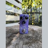 Fialový kytarový efekt s nápisem DAMP Reverb a grafickým motivem hor. Na horní straně jsou tři černé otočné oválné knoflíky s popisky DECAY, LEVEL a…