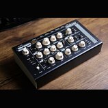 Černý efektový pedál v kovovém šasi s bílými otočnými knoflíky. Na horní straně je nápis „RETROsynth lancet“ a v pravém horním rohu značka „VERONA“.…