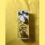 Žlutý kytarový efekt s bílým rámem. Na horní straně jsou tři kovové otočné knoflíky s popisky DRIVE, DRY BLEND a VOLUME, uprostřed je bílý plastový p…
