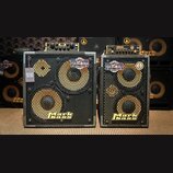 Dvě basové reproduktorové skříně značky Mark bass v černé barvě s kovovými mřížkami. Levá skříň má dva reproduktory a nálepy s nápisy 17,5 kg / 38,6…