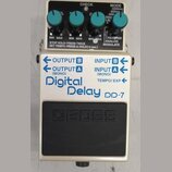 Kytarový efekt pedál značky BOSS, model Digital Delay DP-7. Zařízení má bílé tělo s modrými nápisy a čtyři tyrkysové ovrtovací knoflíky. Na horním če…