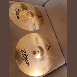 Dvě mosazné činely značky Zildjian. Oba mají nápis CUSTOM a logo ve tvaru písmena A. Spodní činel má v dolní části drobný nečitelný text a technické…
