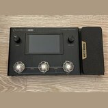 Černý efektový procesor s nápisem AMPERO ONE a doplňkem Amp Modeler / Effects Processor. Zařízení má centrální displej, dva otočné knoflíky s popisky…