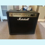 Černý kytarový kombo zesilovač s látkovou mřížkou. Na přední straně je bílé logo Marshall a na ovládacím panelu nápis MG 100W. Panel obsahuje řadu ot…