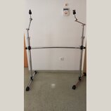 Kromě bílé stěny a šedé podlahy je na fotografii kovový, chromovaný stojan s dvěma vertikálními nohami a vodorovnou spojovací hříčkou. Horní části st…