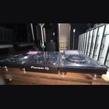 Sada DJského vybavení v černé barvě složená ze dvou kontrolérů s jogovými koly a centrálního mixeru. Na přední straně mixeru je bílý nápis Pioneer DJ…
