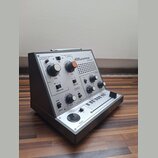 Stříbrný elektronický nástroj s nápisem Stylophone THEREMIN. Přední panel obsahuje několik otočných knoflíků s popisky PITCH, MIX, DECAY a TIME, přep…