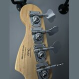 Zadní strana hlavy basové kytary z přírodního dřeva se čtyřmi chromovanými ladičkami. Na dřevě je černý nápis: Designed and Backed by Fender, Crafted…