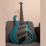 Modrá basová kytara s pětistrunným hmatníkem a dvěma humbuckery. Tělo má matný povrch s tmavším stínováním v oblasti středové části. Na těle jsou umí…