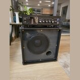 Černý kytarový kombo zesilovač s reproduktorem za kovovou mřížkou a basreflexním otvorem. Horní ovládací panel obsahuje nápisy TUNE GAIN, BASS, MID a…
