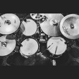 Černobílá fotografie z pohledu bubeníka na bicí sadu. Na čínalech jsou viditelná loga Zildjian a Sabian, na blanách bubnů nápisy EVANS a ETAMA. Sníme…