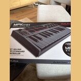 Fotografie zachicuje krabici s produktem AKAI MPKmini SPECIAL EDITION GREY. Na obalu je zobrazen šedý kompaktní MIDI kontrolér s klávesami, osmi červ…