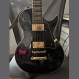 Černá elektrická kytara s gold hardwarem a krémovým lemováním. Na těle jsou dva humbuckery, čtyři ovládací knofíky a přepínač s nápisy RHYTHM a TREBL…