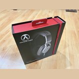 Černá cardboardová krabice s červenými prvky a úchytkou v horní části. Na přední straně je bílé logo a nápis AUSTRIAN AUDIO, fotografie sluchátek a v…