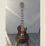 Hnědá elektrická kytara s tvarem singlecut a tmavým hracím hředcem. Na hlavě je bílé logo Gibson a nápis Made in USA. Kytara má dva humbuckery, čtyři…