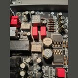 Detailní záběr na elektronickou základovou desku s různými komponenty, jako jsou kondenzátory, rezistory a integrované obvody. Na desce je viditelné…