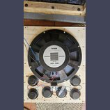Na dřevěné desce je umístěn velký černý reproduktor s magnetem. Na středovém bílém štítku je nápis TESLA, MADE IN CZECHOSLOVAKIA, 50 W-8Ω a ARM 9308,…