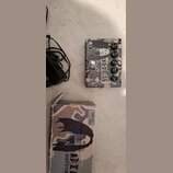 Kytarový efekt pedál s kamuflážním vzorem a černobílým portrétem osoby. Na pedálu je nápis DIME DISTORTION a logo MXR. Vedle pedálu je černý napájecí…