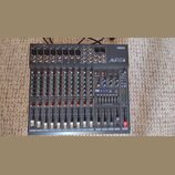 Šedý mixovací pult s nápisy YAMAHA a Mx12/4. Zařízení obsahuje několik vstupních kanálů s posuvníky, knoflíky a červenými kontrolkami. V pravé části…