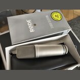 Stříbrný kondenzátorový mikrofon s kovovou síťkou, na jehož těle je nápis Made in Australia. Mikrofon leží v bílém boxu na černém koženěném pouzdře.…