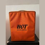 Oranžový textilní kryt na hudební zesilovač. Uprostřed je černý nápis HOT® a pod ním menší text true tube amplifiers. Kryt vykazuje mírné opotřebení…