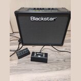 Černý kytarový kombo zesilovač s bílým logem Blackstar na přední mřížce. Před ním leží černý dvoupedálový spínací jednotka s nápisy Blackstar, CHANGE…