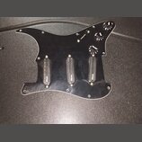 Černý plastový pickguard pro kytaru s třemi černými snímači. Na každém ze snímačů je bílý nápis "Wilkinson". Součástí jsou tři černé ovládací knofíky…