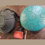 Zelený steel tongue drum s vyrytými čísly 1 až 10 a centrálním logem LENA v ornamentálním kruhu. K nástroji patří černý přepravní vak, dva dřevěné pa…