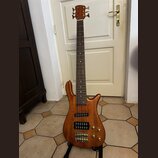 Šeststrunná basová kytara s přírodním dřevěným povrchem a hnědým hmatníkem. Na těle jsou umístěny dva humbuckery, čtyři zlaté potenciometry a zlatý m…