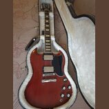 Elektrická kytara s červeným trupem a černým pickguardem v otevřeném hnědém kufru s bílou vnitřní výplní. Na hlavě kytary je viditelné logo Epiphone.…