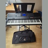 Černý digitální klavír značky YAMAHA, model PSR-E453, umístěný na černém X-stojanu. Nástroj má bílé a černé klávesy, displej a ovládací tlačítka. Pře…