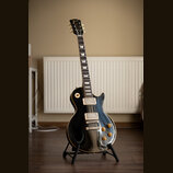 Černá elektrická kytara s jednovýstupním tělem a hnědým lemováním. Na hlavě je zlatý nápis Gibson. Kytara má dva humbuckery, čtyři otočné knoflíky a…