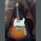 Elektrická kytara s tělem v barvě sunburst a bílým pickguardem, položená na černém obalu. Na hlavě hředu je viditelné logo "Ltd". Nástroj vykazuje zn…
