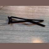 Černý kovový stojan nebo držák s rozkládací konstrukcí. Předmět je položen na šedém povrchu s texturou dřeva. Na fotografii nejsou viditelné žádné zn…