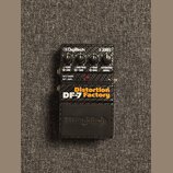 Kytarový efekt pedál značky Digitech z řady X SERIES. Na čelní straně je oranžový nápis Distortion DF-7 Factory a čtyři ovládací knofíky s popisky LE…