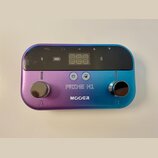 Multiefektový pedál v kovovém provedení s barevným přechodem od fialové k modré. Na horní straně je černý displej s ikonami baterie a Bluetooth, pod…