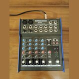 Mixážní pult s modrým šasi a stříbrným předním panelem. Na horní části je nápis PRONOMIC M-602 PREMIUM 6-INPUT 2-BUS MIXER. Zařízení obsahuje různé v…