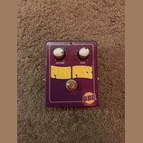 Fialový kytarový efekt s dvěma bílými otočnými knoflíky. Na šasi jsou nápisy VOLUME a FUZZ s číslováním 0–10, velký žlutý nápis FREE FUZZ TM a v prav…